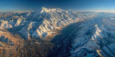 Snow-covered mountains tower over a valley near a city during golden hour in the early evening photo