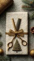 Gift wrapped in white with golden scissors and a small Christmas tree decor on a textured surface photo