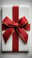Elegant white gift box adorned with a red ribbon sits against a textured wall, ready for a special occasion or celebration photo