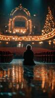 Person sitting alone in an empty theater surrounded by strings of lights during a quiet evening photo