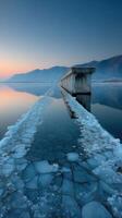 Frozen lake at dawn with an old pier and fragmented ice near mountains photo