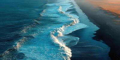 Waves crashing on sandy beach at sunset reflecting hues of blue and orange over calm ocean surface photo