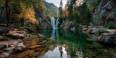 Scenic waterfall cascades into tranquil pool surrounded by autumn foliage in a forested landscape photo