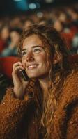 Young woman smiles while talking on the phone in a theater filled with an audience during a movie screening photo