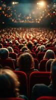 Audience watches a live performance in an auditorium with red seating and dimmed lights during an evening event photo