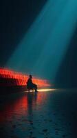 Lonely figure sitting in a dimly lit space with blue and red reflections during a quiet evening photo