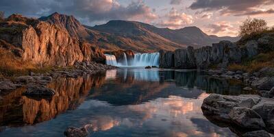 Stunning waterfall cascades into serene lake surrounded by rugged mountains during sunset in a peaceful landscape photo