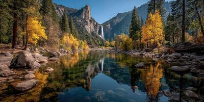 Autumn reflection on a calm river with golden trees and mountains in the background under a clear blue sky photo