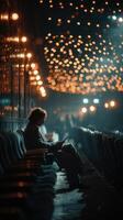 Evening ambiance with a solitary figure immersed in digital content at a dimly lit venue filled with twinkling lights photo