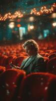Young man engages with his smartphone while seated in a nearly empty theater during a performance photo