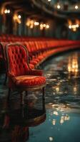 Empty red chair reflects in water at an abandoned theater during twilight hours with warm lights in the background photo