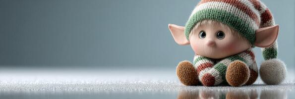 Cute elf doll wearing a striped hat and scarf sitting on a shiny surface at a cozy indoor location during winter photo