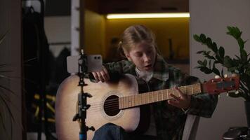 Caucasian little girl learning play guitar looking online tutorial mobile phone student talented child kid study song learn playing music watch lesson smartphone camera tripod teacher call sing video