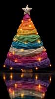 Colorful yarn Christmas tree with twinkling lights displayed on a reflective surface during the holiday season photo