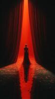 Elegant figure stands in a dramatic red-lit setting with flowing curtains and reflective floor during a theatrical performance photo