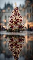 Festively decorated Christmas tree with red and gold ornaments reflects on wet surface in a city square during winter photo