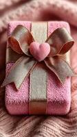 Delicate pink gift box wrapped in satin ribbon with heart-shaped embellishment on soft, textured background photo