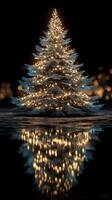 Decorative Christmas tree with glowing lights reflecting on a surface in a dark setting during the holiday season photo