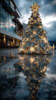 Decorative Christmas tree adorned with lights and ornaments reflects on wet pavement in urban courtyard during winter evening photo