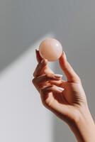 Hand holding a smooth pink crystal sphere against a soft gradient background, showcasing the delicate texture and natural beauty of the stone, emphasizing wellness and mindfulness concepts photo
