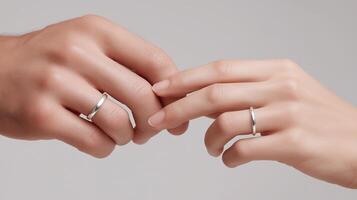 Close-up of two hands gently touching, adorned with elegant silver rings, symbolizing love and commitment, against a soft neutral background, creating a romantic and intimate atmosphere photo