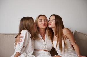 Happy Mother With Two Daughters Sharing Affection on a Sofa in a Bright Room photo