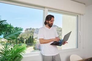 Bearded Man in Casual Outfit Working on Laptop in Modern Home Office with Scenic Views photo