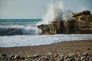 Large Ocean Wave Crashing Against Coastal Rock Formation on a Pebble Beach photo