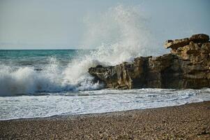 Serene Ocean Waves Crashing Against Coastal Rock Formations on a Pebbled Beach photo