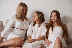 Mother and Two Daughters Smiling and Conversing on a Sofa in a Warm Family Moment photo