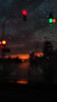 Blurred view through rain-soaked windshield capturing traffic lights glowing against dark stormy sky with hints of sunset creating dramatic urban atmosphere photo