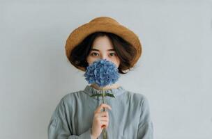 A woman wearing a hat and holding a blue flower photo