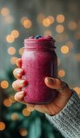 A woman holding a jar of smoothie in front of a christmas tree photo