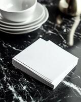Stack Of White Napkins On A Black Marble Surface With White Dishes photo
