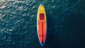 Aerial View of a Yellow and Red Paddleboard on Dark Blue Water photo