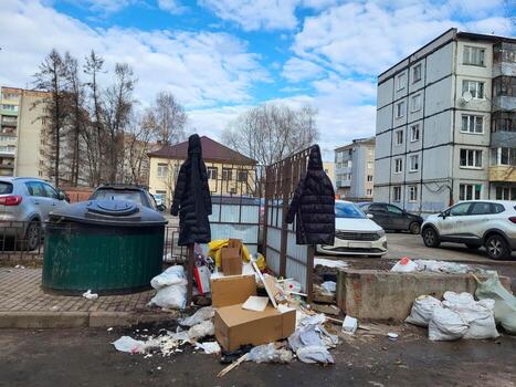 Garbage is piled up, two coats are hanging on the fence past the waste containers. Violation of the rules of garbage disposal. photo