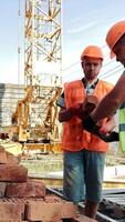 two men in orange vests and hard hats are working on bricks video