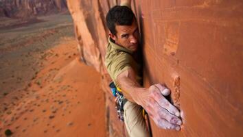 Man climbs a rocky wall in a desert landscape during daytime in an adventurous outdoor setting close to towering red cliffs photo
