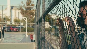 Unhealthy Sick Man with Protection Mask Watching Basketball Players in a Basketball Field Behind the Metallic Fence video