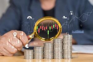 Stack of money coin and magnifying glass with graph and candle stick chart. photo