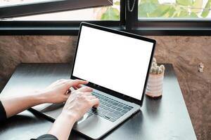 Hands typing on a laptop with a blank screen in a modern workspace by a window, featuring natural light and minimalist decor. photo