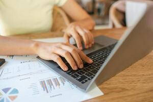 Close-up of hands typing on a laptop with financial documents on a wooden desk, showcasing a productive work environment. photo