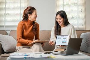 Two women discussing work, using a digital tablet and documents in a well-lit modern office space. photo
