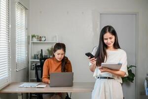 Two women in a home office, one using a laptop and the other with a smartphone and notebook, showcasing modern work dynamics. photo