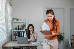 Two women working together in a bright office, using laptops and reviewing documents, showcasing teamwork and productivity. photo