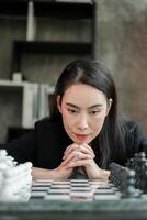 Woman deeply focused on a chess game, contemplating her next move in a modern room with a bookshelf. photo