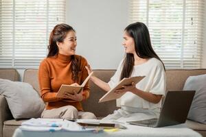 Two women engaged in a friendly discussion, working together on a project with laptops and notebooks in a comfortable living room. photo