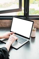 Hands typing on a laptop with a blank screen, set by a window in a bright, modern workspace. photo