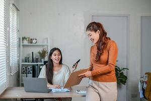 Two women working together in a modern office, using laptops and documents, fostering a collaborative and productive atmosphere. photo