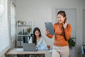 Two women working together in a modern office, using technology and reviewing documents, showcasing teamwork and productivity. photo